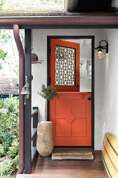 an orange front door on a house with a surfboard in the foreground and a potted plant next to it