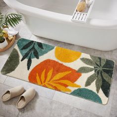 a bathroom rug with flowers on it next to slippers and a bathtub in the background