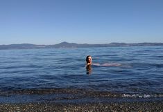 a woman swimming in the ocean with her head above water and mountains in the background