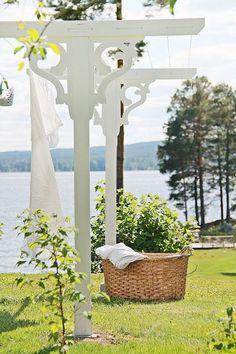 a basket sitting under a white arbor in the grass next to a body of water