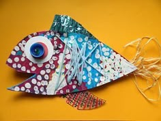 a colorful fish made out of paper on a yellow surface with white polka dots and blue eyeballs