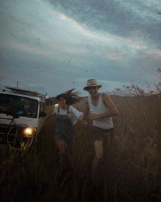 two people running through tall grass with a truck in the background