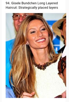 a woman with long hair smiling and wearing a white top in front of a crowd