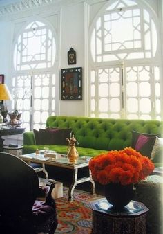 a living room with green couches and orange flowers in vases on the coffee table