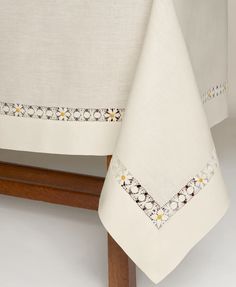 a white table cloth on top of a wooden stand with an embroidered border around it