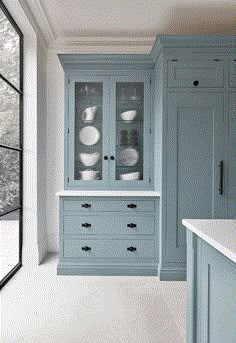 an empty kitchen with blue cabinets and white counter tops, in front of a large window