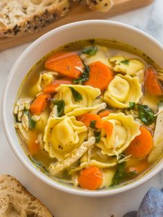 a white bowl filled with chicken noodle soup next to a piece of bread on a table