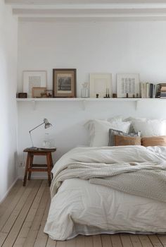 a bedroom with white walls and wooden flooring is pictured in this image, there are books on the shelves above the bed