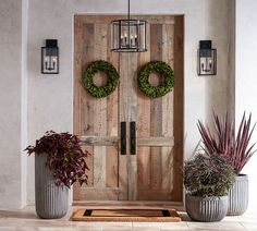 two potted plants sit in front of a wooden door with wreaths on it