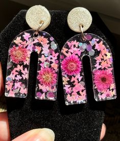 a pair of earrings with pink flowers and glitters on the bottom are being held up