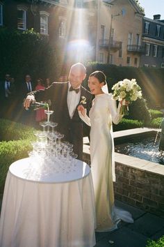 a bride and groom standing next to a table with wine glasses on it in front of a fountain