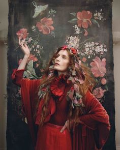 a woman with long red hair wearing a red dress and holding her hands up in the air