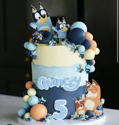 a blue and white cake with cartoon characters on it's top, sitting on a table