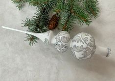 two white and silver ornaments sitting on top of a table next to a pine tree