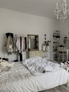 an unmade bed sitting in a bedroom next to a white dresser and chandelier