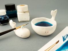 some blue ink is in a white bowl next to two small bottles and a brush