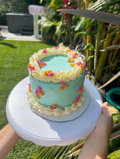 a person holding up a cake with frosting and flowers on it in the backyard