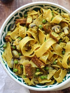 a bowl filled with pasta and peas on top of a wooden table next to a fork