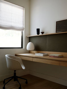 a desk with a lamp and some books on it in front of a large window