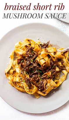 a white plate topped with pasta covered in meat and sauce on top of a table