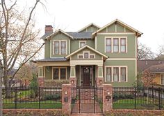 a green house with two story and black iron fence