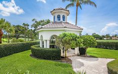 a white gazebo surrounded by lush green grass and palm trees on a sunny day