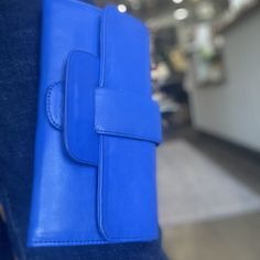 In-house design that came to life through fair trade artisans in Indonesia. Leather wallet with belted closure in blue. Perfect as a wallet, and for a clutch with a pop of color. 9" L x 5" W, tri-fold wallet with snap closure and asthetic buckle. Interior: 19 card slots, large zipper pocket, 3 large slide pockets. Modern Blue Leather Clutch, Everyday Blue Rectangular Clutch, Blue Rectangular Clutch For Everyday, Blue Trifold Wallet With Card Slots For Daily Use, Blue Trifold Wallet With Interior Card Slots, Blue Rectangular Wallet With Cell Phone Pocket, Blue Rectangular Wallet For Everyday Use, Blue Wallets With Interior Card Slots For Daily Use, Rectangular Blue Wallet For Everyday Use