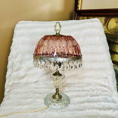 a pink glass lamp sitting on top of a white blanket