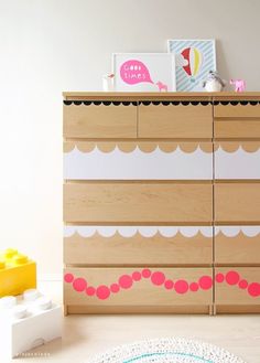 a child's dresser with pink and white trim on the top, next to a yellow toy car