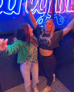 two girls standing in front of a neon sign