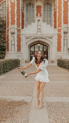 a woman in a white dress is holding a bottle and posing for the camera with her legs spread out