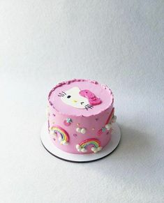 a pink hello kitty cake with rainbows and clouds