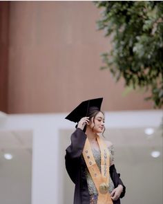 a woman wearing a graduation gown and holding a cell phone to her ear while standing in front of a building