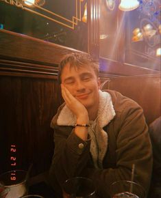 a young man sitting at a table with his hand on his face and looking to the side