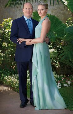 a man and woman standing next to each other in front of trees, bushes and flowers