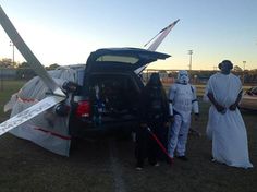 some people in costumes standing next to a car with an airplane on it's back