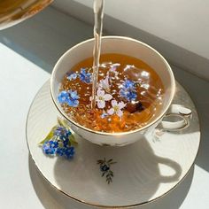 a bowl of soup being poured into it with blue flowers on the side and a spoon