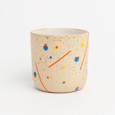 a white cup with orange, blue and yellow speckles on the outside of it