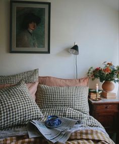 a bed covered in pillows and blankets next to a window with a painting on the wall