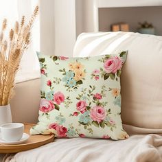 a flowered pillow sitting on top of a white couch next to a cup and saucer