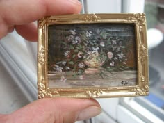 a person holding up a miniature painting with flowers in the middle and on it's side