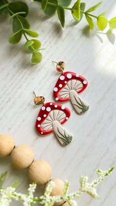 two red and white earrings sitting on top of a table next to green leaves,