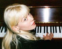 a blonde woman sitting at a piano with her hand on the keys and looking up