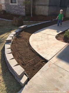 a little boy standing in the middle of a yard next to a sidewalk and flower bed