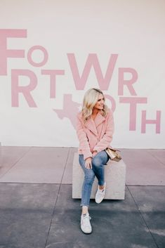 a woman sitting on top of a cement block in front of a pink and white sign