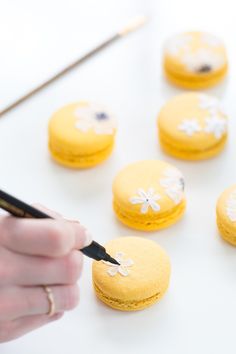 a person using a pen to draw flowers on yellow macaroons