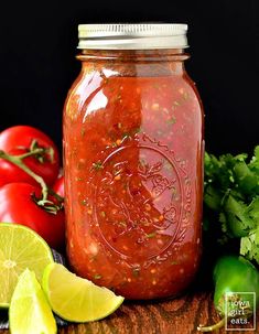 a glass jar filled with salsa next to limes and tomatoes