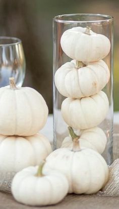 small white pumpkins are stacked on top of each other in front of a wine glass