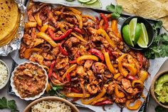 an assortment of food is laid out on a table with tortillas, limes and salsa