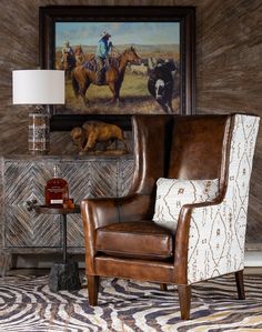 a chair in front of a painting on the wall with a cow and cowboy scene